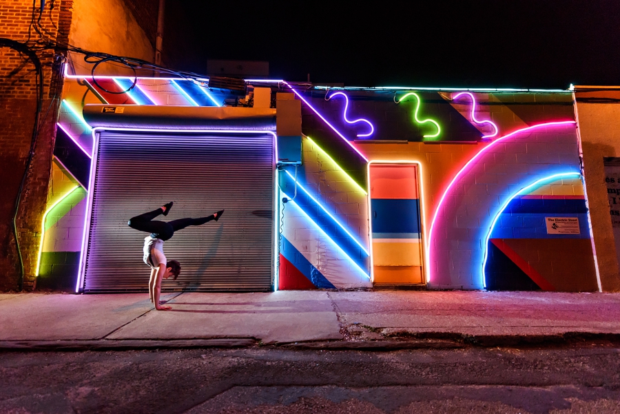 A woman doing a handstand in philadelphia in front of neon light graffiti.